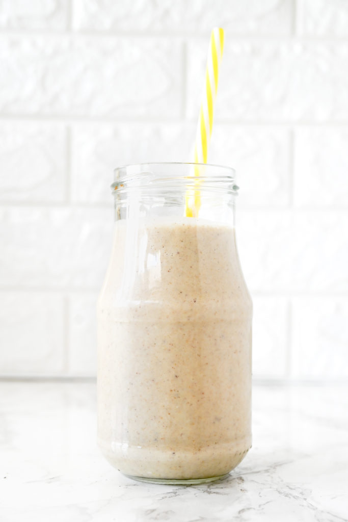 Banana Smoothie with Oat Milk in a glass with a yellow straw on a white marble counter