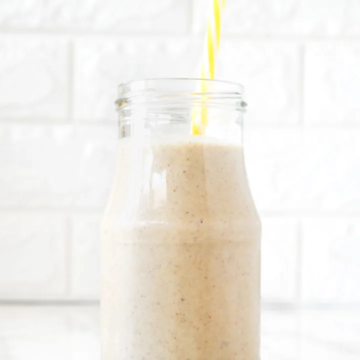 Banana Smoothie with Oat Milk in a glass with a yellow straw on a white marble counter