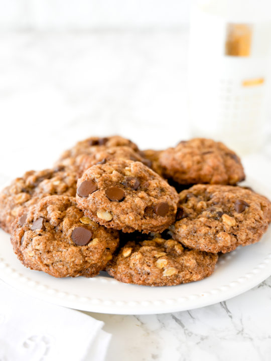 Chocolate chip oatmeal cookies on a plate on a marble counter next to a glass