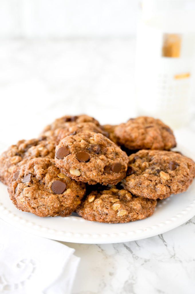Chocolate chip oatmeal cookies on a plate on a marble counter next to a glass