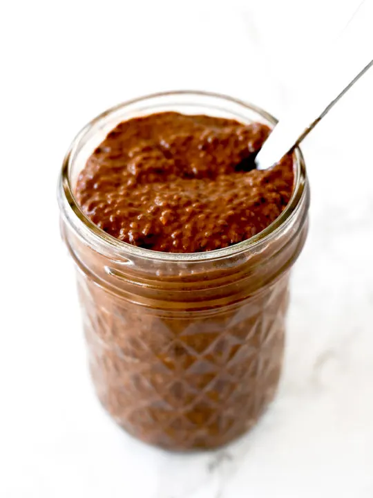 Chocolate chia pudding in a mason jar with a spoon on a white marble counter