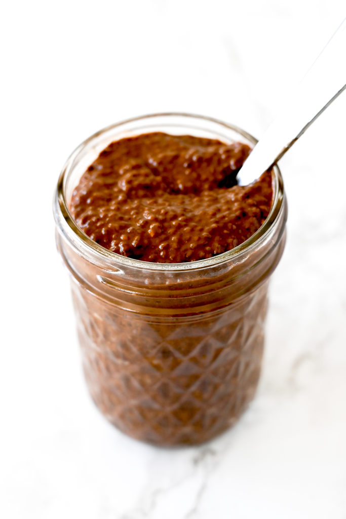 Chocolate chia pudding in a mason jar with a spoon on a white marble counter