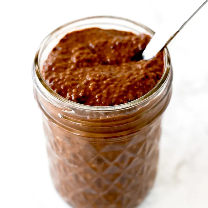 Chocolate chia pudding in a mason jar with a spoon on a white marble counter