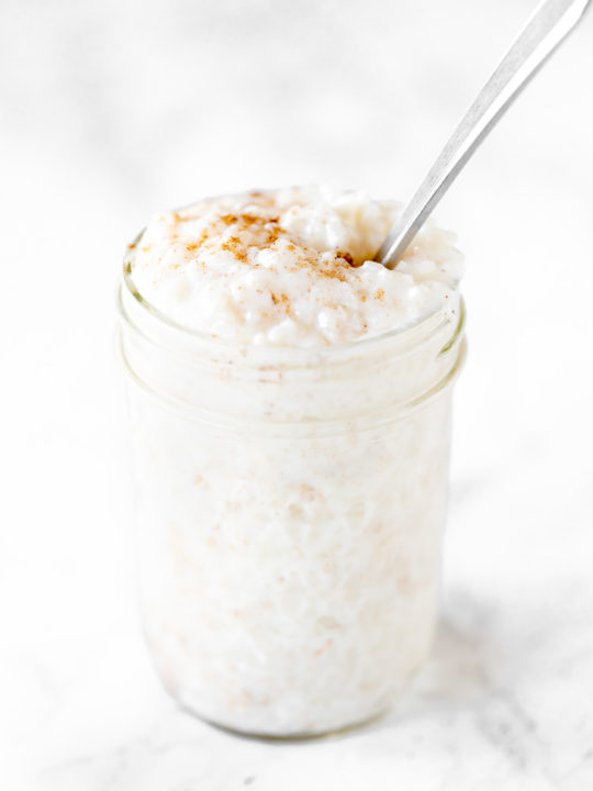 dairy free rice pudding in a mason jar with a spoon on a white marble counter