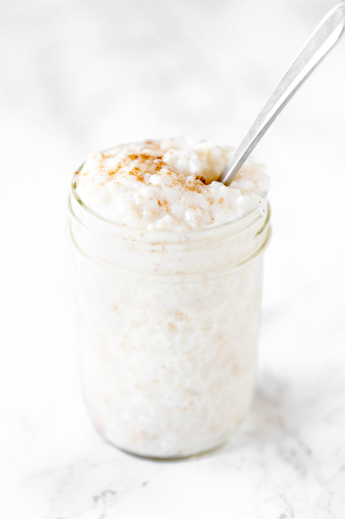 dairy free rice pudding in a mason jar with a spoon on a white marble counter