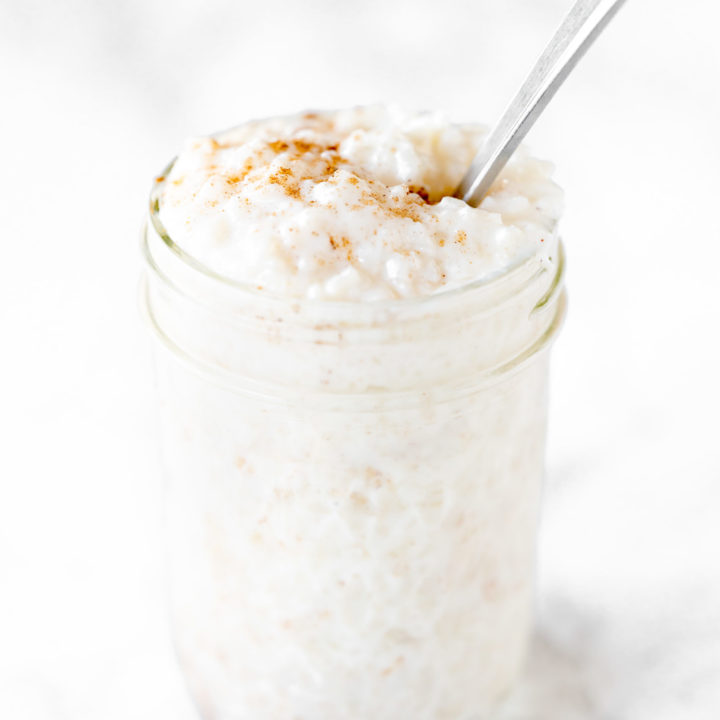 dairy free rice pudding in a mason jar with a spoon on a white marble counter
