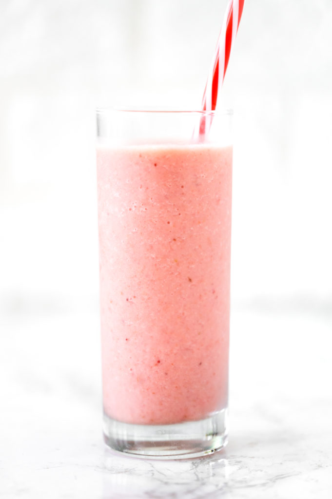 strawberry banana smoothie with oat milk in a glass with a red straw on a white marble counter
