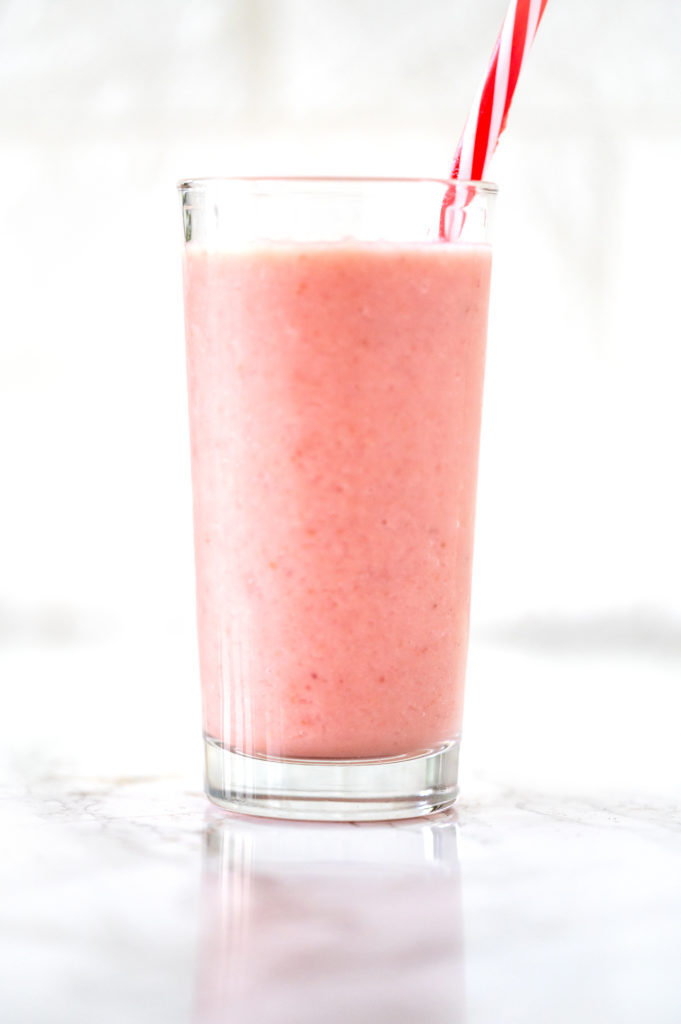 dairy free strawberry banana smoothie in a class with a red straw on a white marble counter