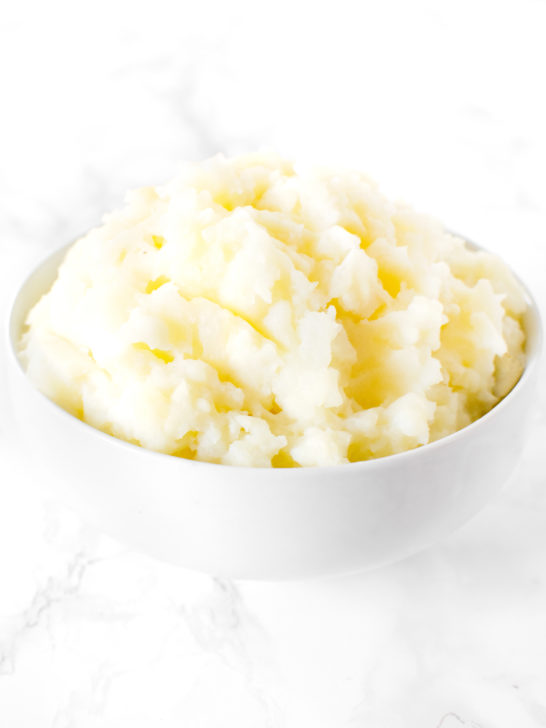 A mound of mashed Potatoes in a white bowl on a white marble counter