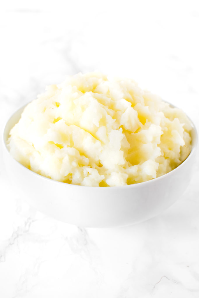 A mound of mashed Potatoes in a white bowl on a white marble counter