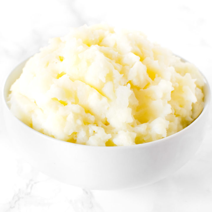 A mound of mashed Potatoes in a white bowl on a white marble counter