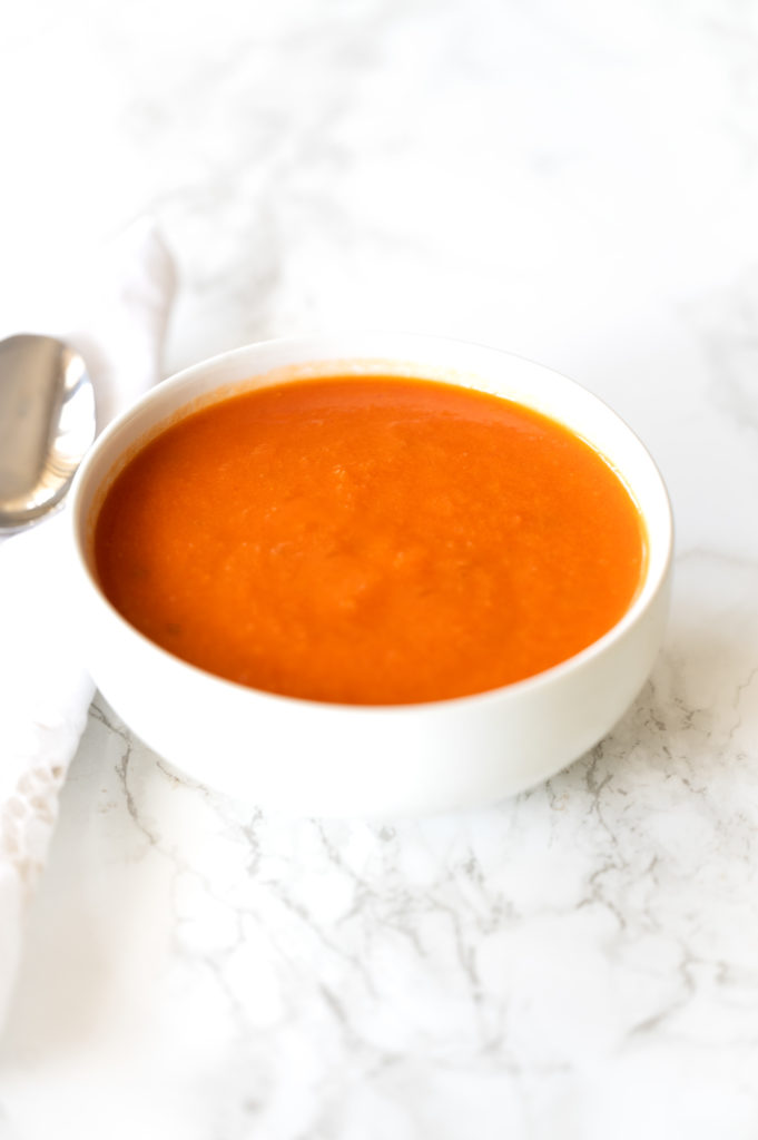 Dairy free tomato soup in a white bowl on a white marble counter