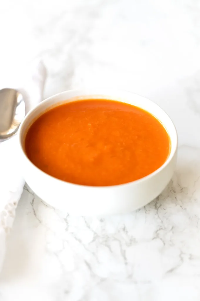 Dairy free tomato soup in a white bowl on a white marble counter
