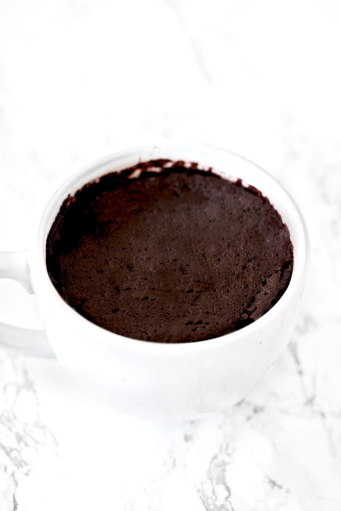 chocolate mug cake in a white mug on a white marble counter