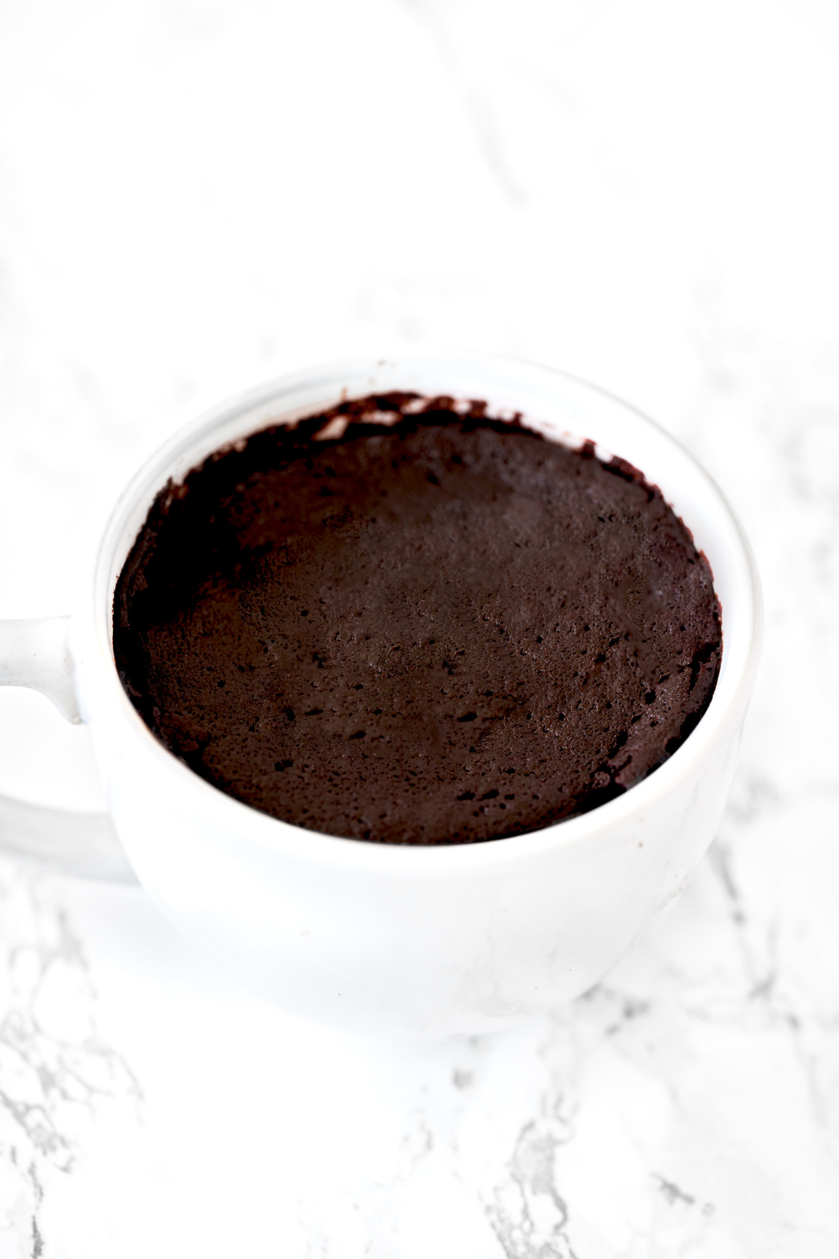 chocolate mug cake in a white mug on a white marble counter