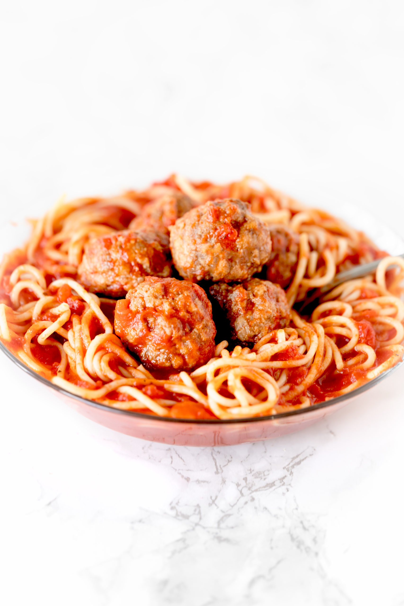 meatballs in a bowl of spaghetti on a white marble counter
