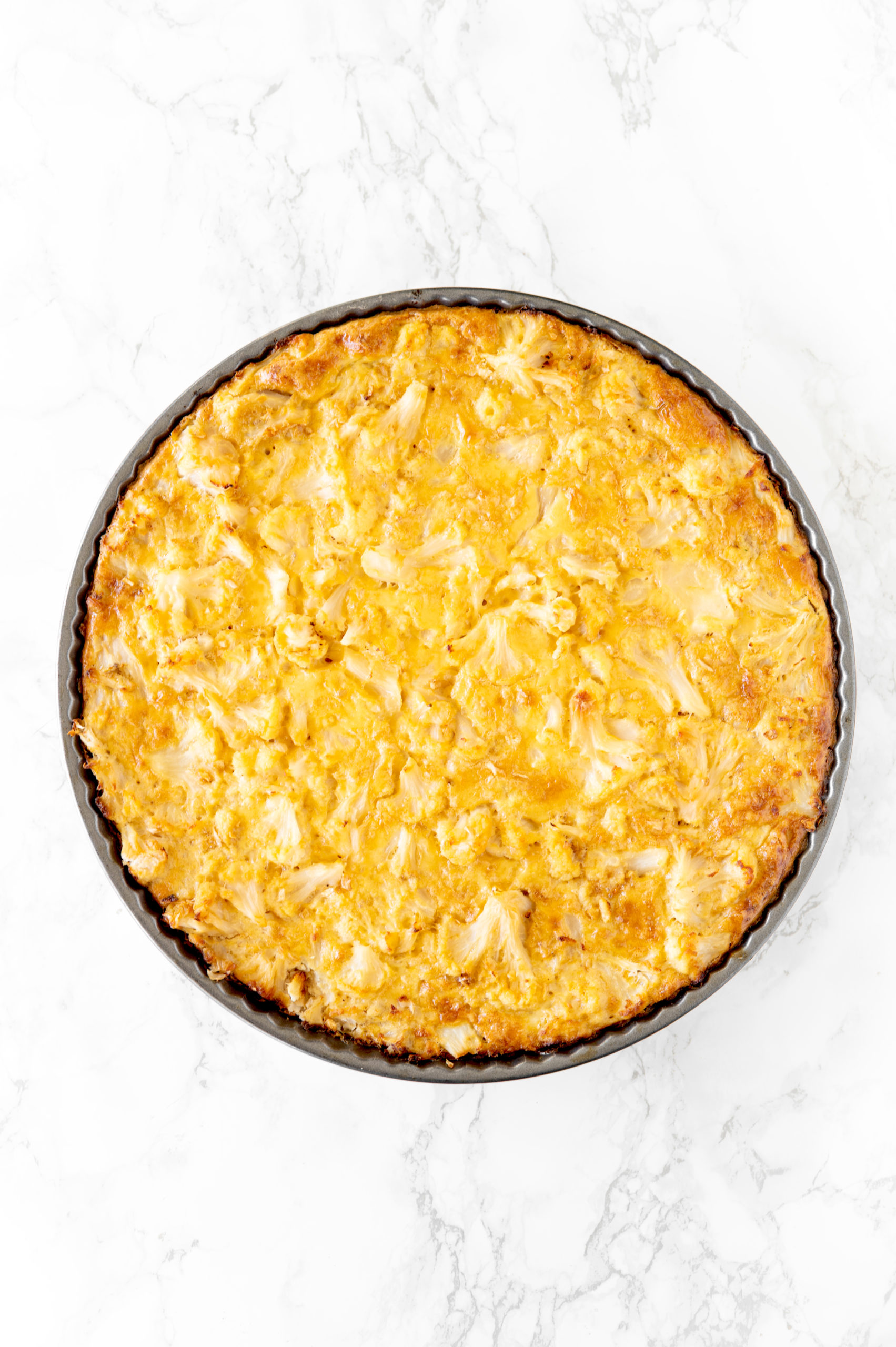 cauliflower kugel in a round pan on a white marble counter