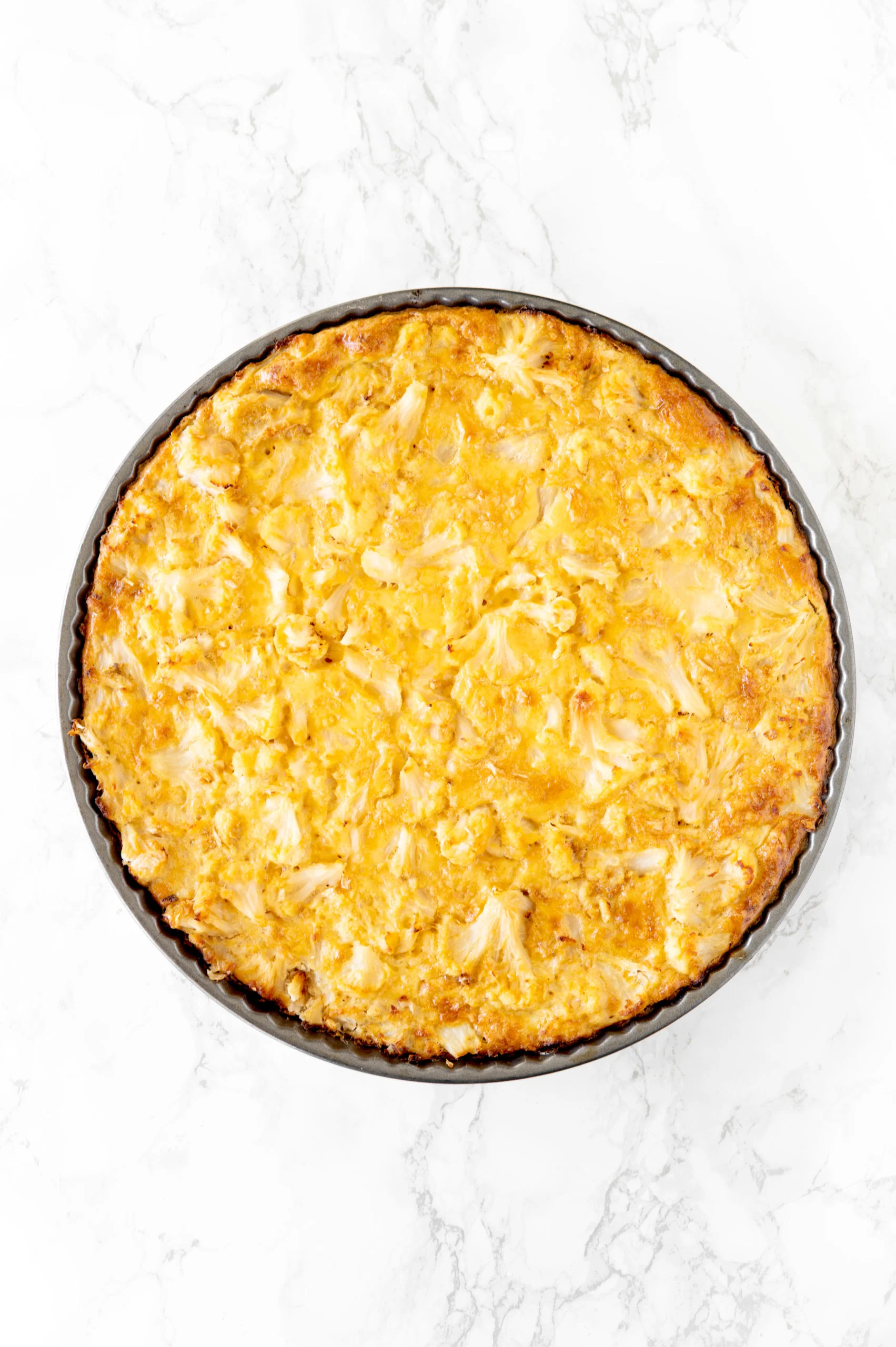 cauliflower kugel in a round pan on a white marble counter
