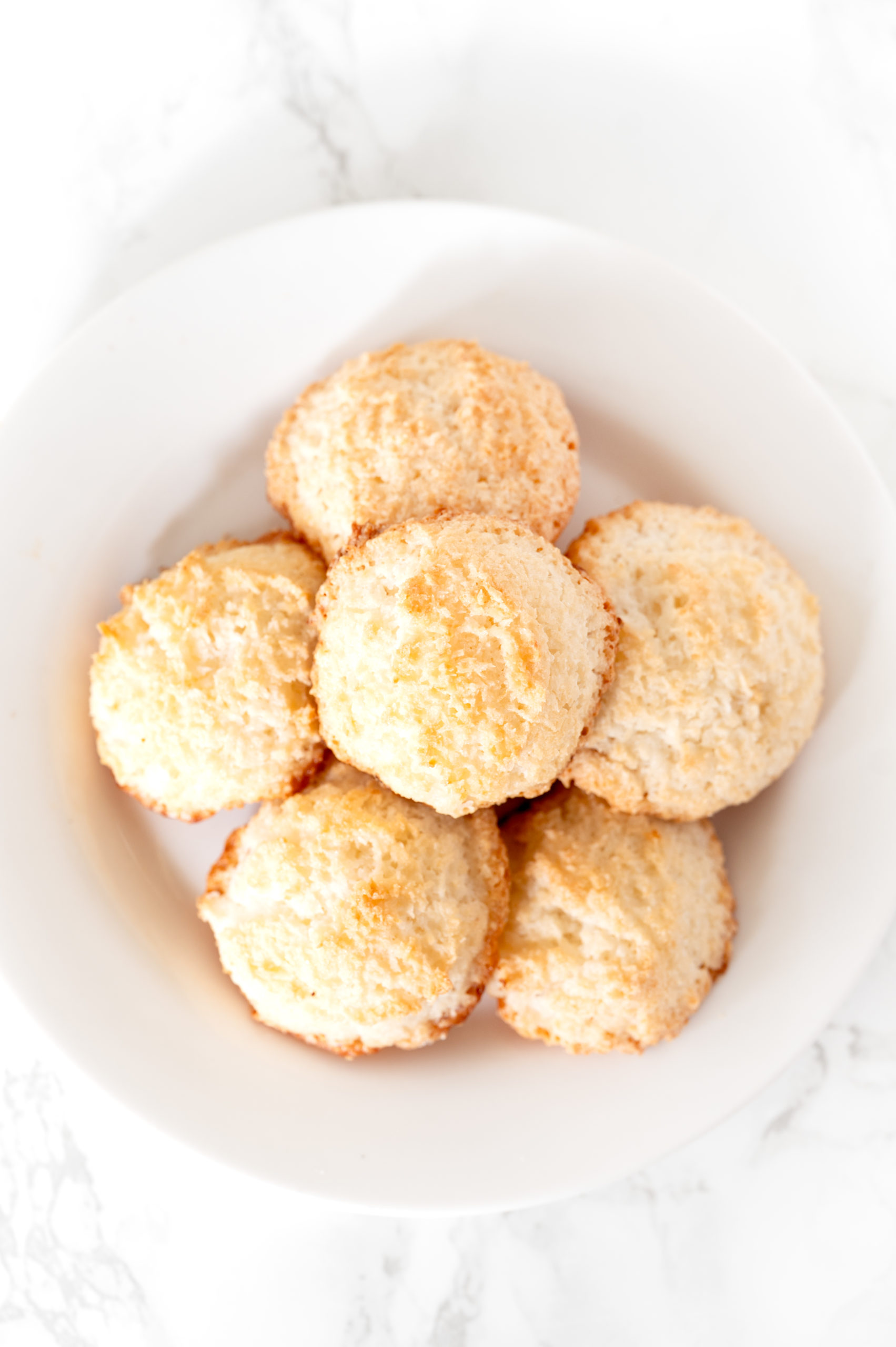 coconut macaroons made without condensed milk sitting on a white plate on a white marble counter