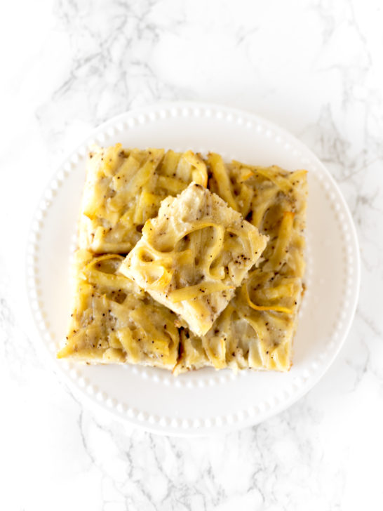 salt and pepper kugel cut into slices, stacked on a plate, on a white marble counter