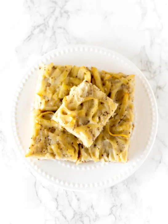 salt and pepper kugel cut into slices, stacked on a plate, on a white marble counter