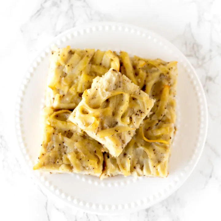 salt and pepper kugel cut into slices, stacked on a plate, on a white marble counter
