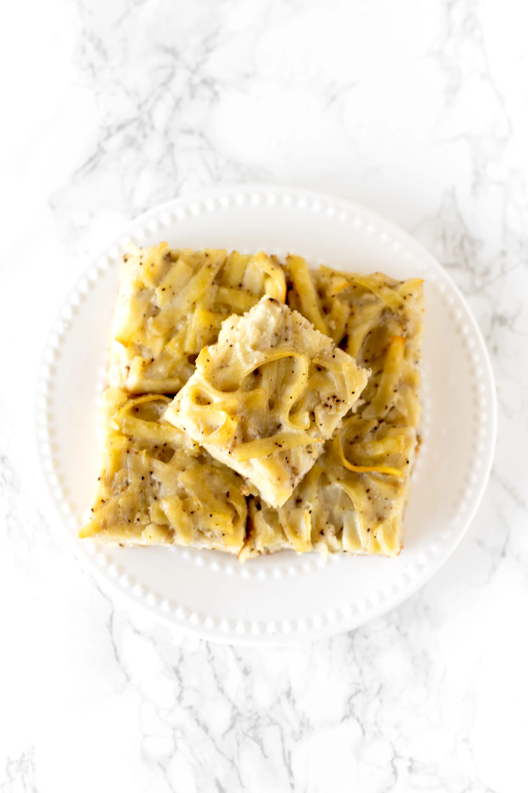 salt and pepper kugel cut into slices, stacked on a plate, on a white marble counter